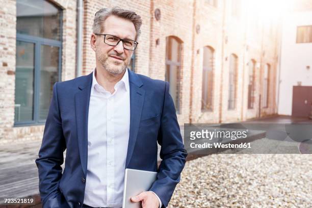 portrait of businessman with tablet wearing glasses and blue jacket - mann anzug gebäude objekt draussen stock-fotos und bilder