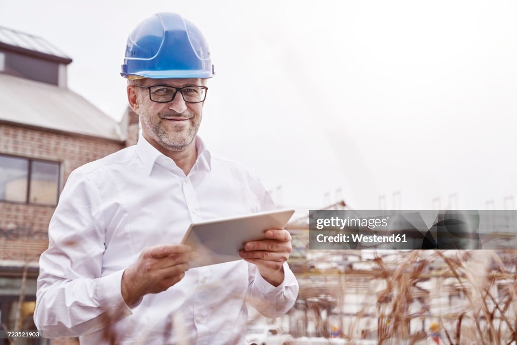 Portrait of smiling man with tablet wearing blue hart hat