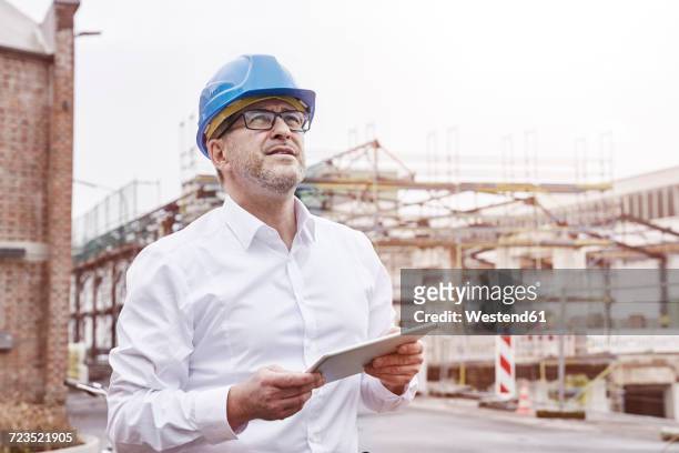 portrait of smiling man with tablet wearing blue hart hat - architect industrie stock-fotos und bilder