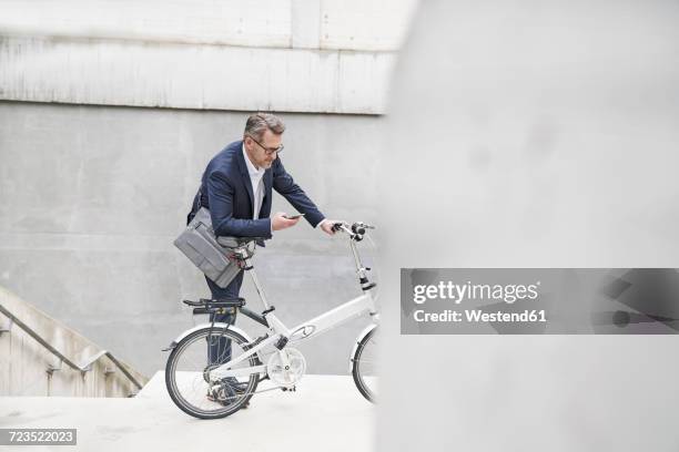 businessman with folding bicycle looking at cell phone - zusammenklappbar stock-fotos und bilder