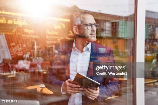 mature businessman in cafe holding tablet - background light stock-fotos und bilder