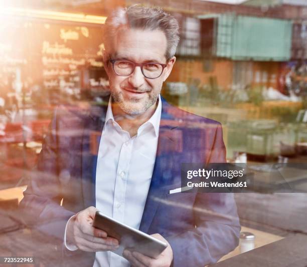 confident mature businessman with tablet looking out of window - view-through-restaurant-window stock pictures, royalty-free photos & images