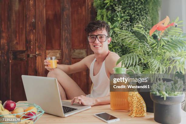 young man using laptop and drinking orange juice at home - freak stock-fotos und bilder