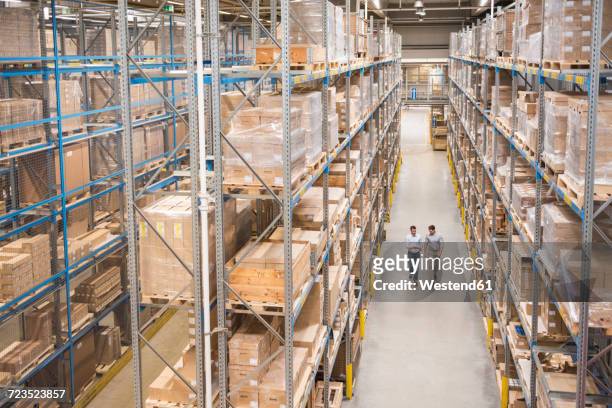 two men walking in factory warehouse - lagerhalle stock-fotos und bilder