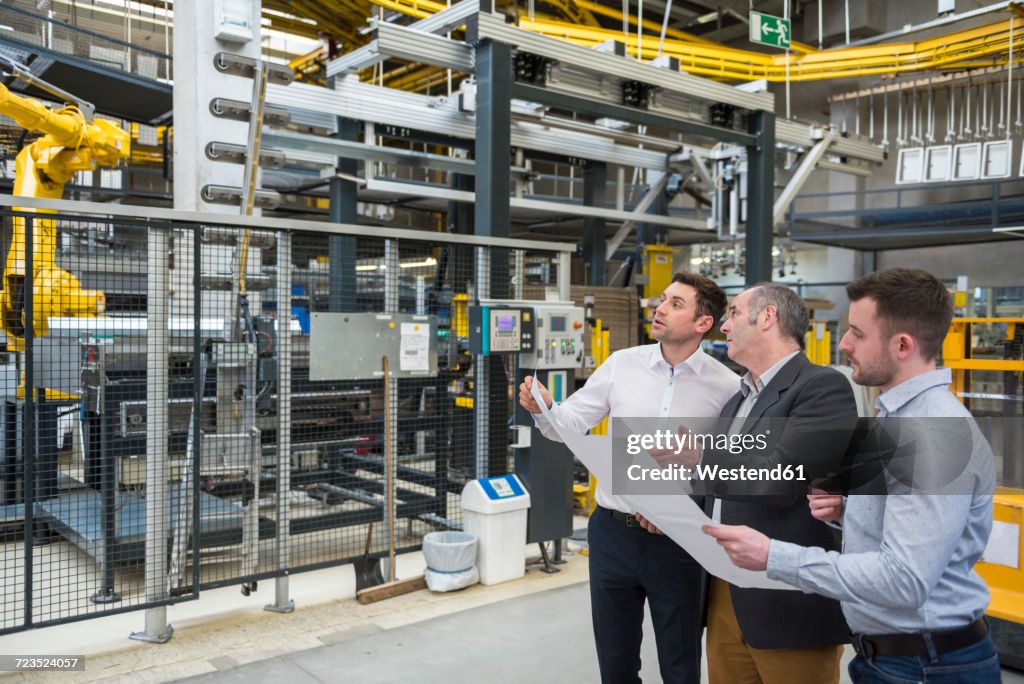 Three men with blueprint talking in factory shop floor