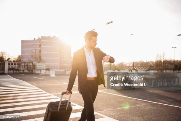 businessman with rolling suitcase checking the time - luggage trolley stock-fotos und bilder