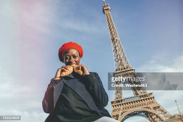 france, paris, young woman eating two croissants in front of eiffel tower - paris millenials stock-fotos und bilder