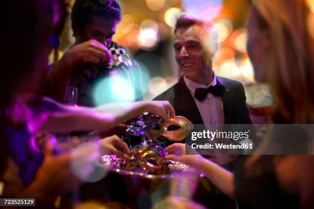 man in tuxedo handing over eye masks on a costume party - elegant party fotografías e imágenes de stock