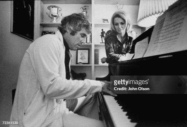 Actress Angie Dickinson watching her husband, composer Burt Bacharach, playing the piano.