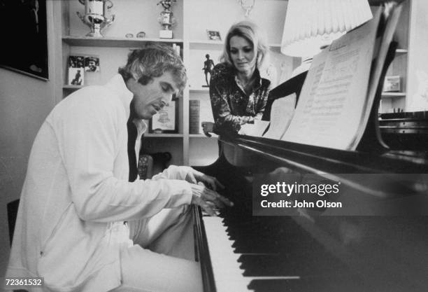 Actress Angie Dickinson watching her husband, composer Burt Bacharach, playing the piano.