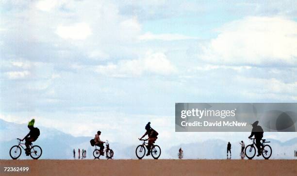 People ride bicycles against a backdrop of mirages September 2, 2000 at the15th annual Burning Man festival in the Black Rock Desert near Gerlach,...