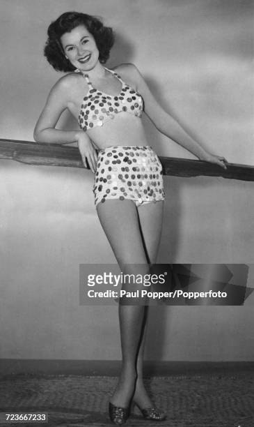American actress Barbara Hale poses wearing a bathing suit adorned with dozens of coins donated by American servicemen stationed around the world,...