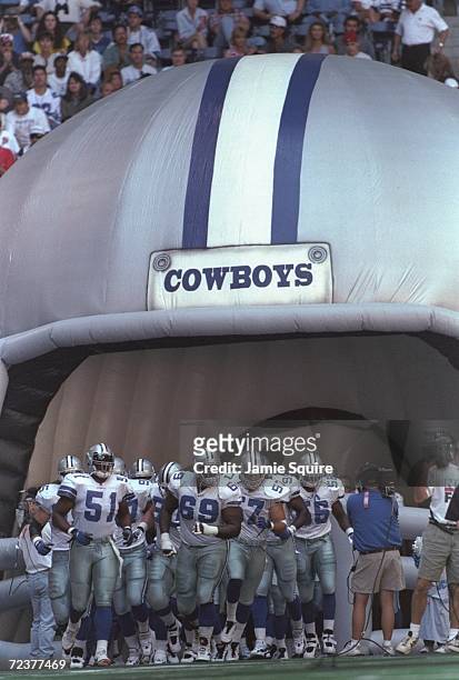 Several members of the Dallas Cowboys emerge through a giant inflatable helmet as they jog out onto the field from the locker room tunnel during the...