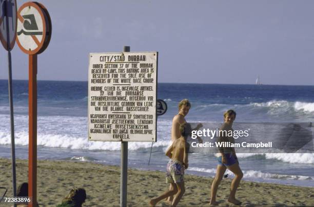 Whites only sign in foreground at restricted beach, with bathers in background.