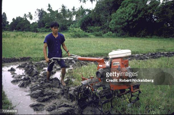 Farmer working in rice paddy with power tiller equipped with locally manufactured Honda engine.