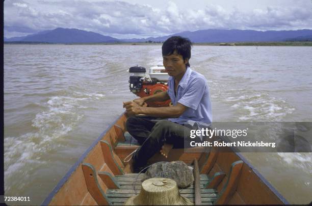 Locally manufactured Honda engine powering long tailed boat propelling man through calm waters of Bhumipol reservoir.