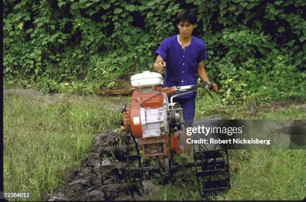 Farmer working in rice paddy with power tiller equipped with locally manufactured Honda engine.