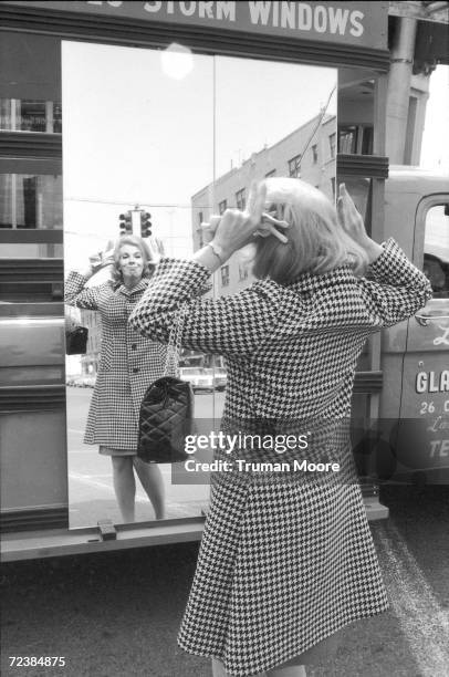 Comedienne Joan Rivers making faces in a mirror on the street. [Scanned from contact sheet.].