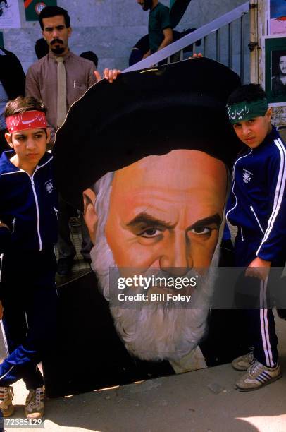 Islamic Scouts, young boys in uniform, hold up large portrait of the Ayatullah Khomeini out side mosque during memorial service for those killed in...