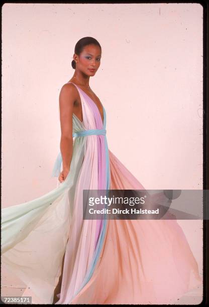 Black model Beverly Johnson shown full length modeling Halston long dress made of pastel vertical pieces of flowing material, probably chiffon which...