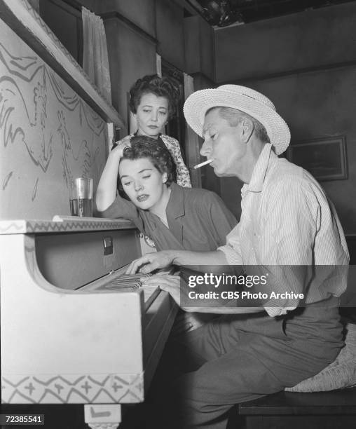 American musicial and actor Hoagy Carmichael , a straw hat on his head and a cigarette in his mouth, plays the piano while Polly Bergen and Sylvia...