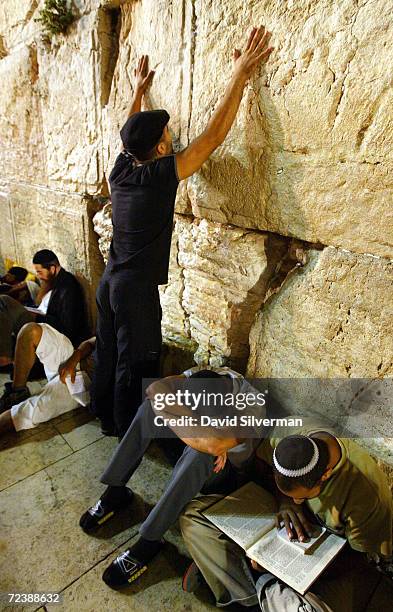 Religious Jew raises his hands in prayer as other worshippers sit alongside him before dawn on the ancient stones of the Western Wall in Jerusalem's...