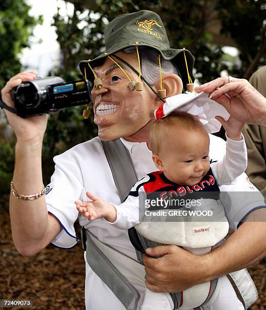 An English fan wearing a mask and an Australian hat, holds his young son as he films while waiting for the England cricket team to walk out of the...