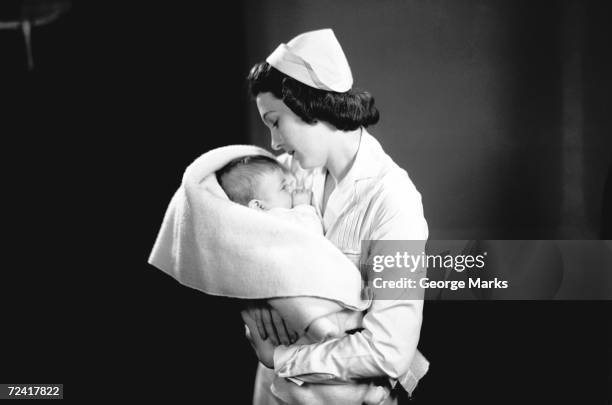 nurse hugging newborn (0-3 months) wrapped in blanket, (b&w) - 20th century stock pictures, royalty-free photos & images