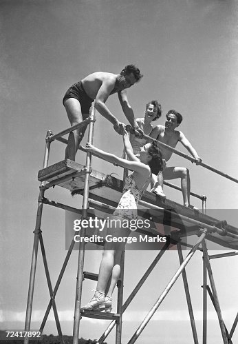 Two couples on springboard, (B&W), low angle view Two couples on springboard, (B&W), low angle view