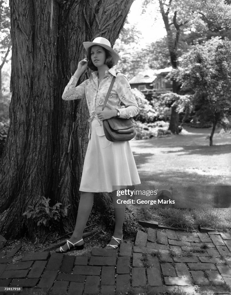 Young woman in hat standing by tree, (B&W),