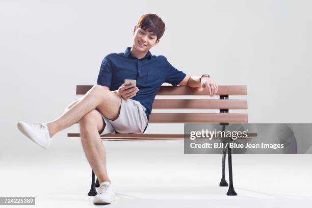 happy young man using smart phone - asian man seated stockfoto's en -beelden