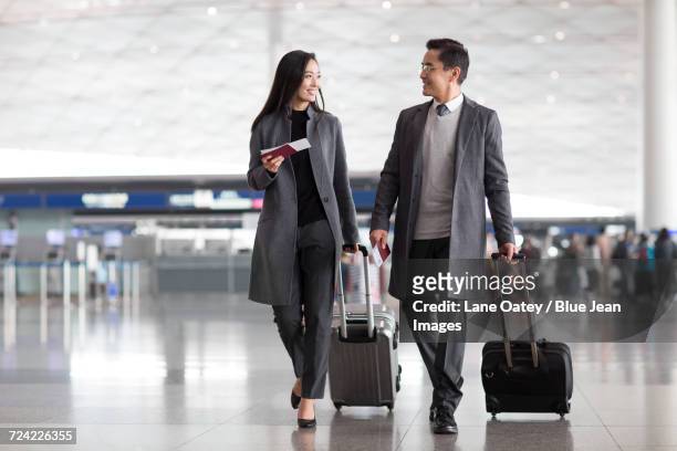 business people pulling wheeled luggage in airport lobby - business travel asian stock pictures, royalty-free photos & images