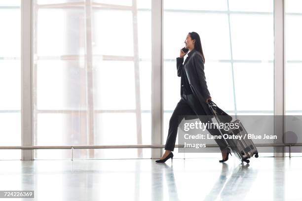 businesswoman pulling wheeled luggage in airport lobby - businesswoman airport stock pictures, royalty-free photos & images