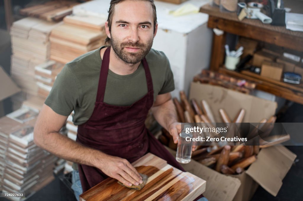 Portrait of man applying wood stain to chopping board in factory