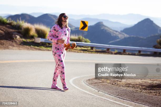 man wearing pink onesie walking in road carrying teddybear, malibu canyon, california, usa - pajamas stock pictures, royalty-free photos & images