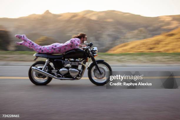 man wearing onesie lying on front riding motorcycle, malibu canyon, california, usa - raro fotografías e imágenes de stock