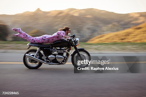Man wearing onesie lying on front riding motorcycle, Malibu Canyon, California, USA Man wearing onesie lying on front riding motorcycle, Malibu Canyon, California, USA