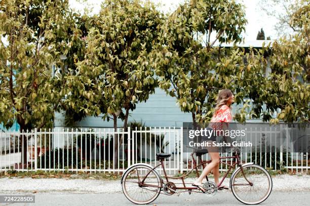 young woman cycling alone on tandem bicycle along street - ciclismo tandem fotografías e imágenes de stock