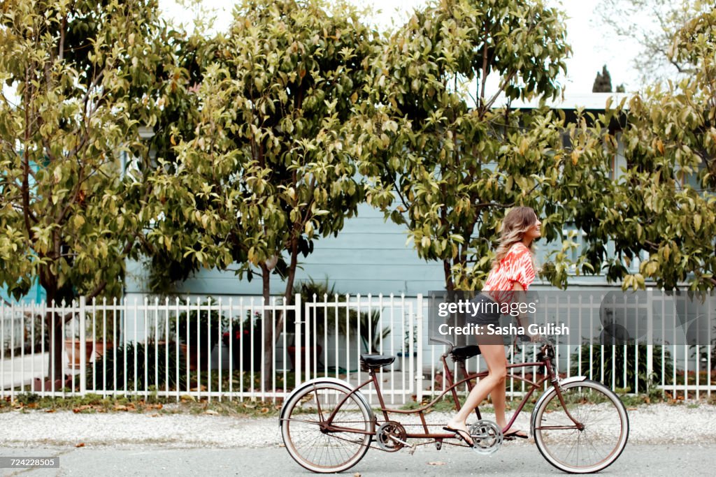 Young woman cycling alone on tandem bicycle along street