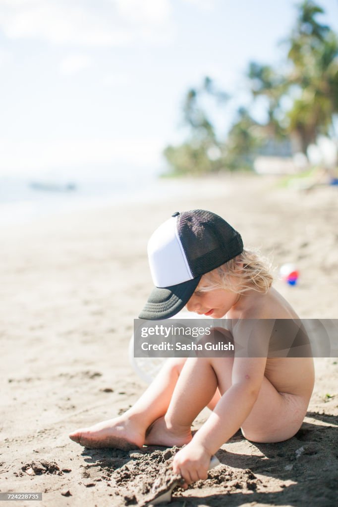 Young boy sitting on beach, digging in sand