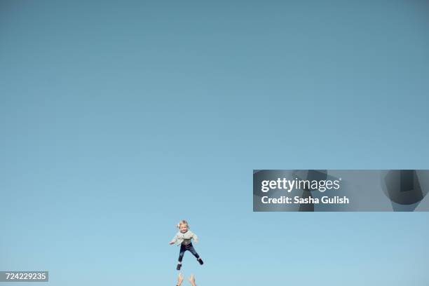 distant view of female toddler thrown mid air against vast blue sky - hand gag foto e immagini stock