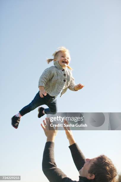 female toddler thrown mid air by father against blue sky - arremessar imagens e fotografias de stock