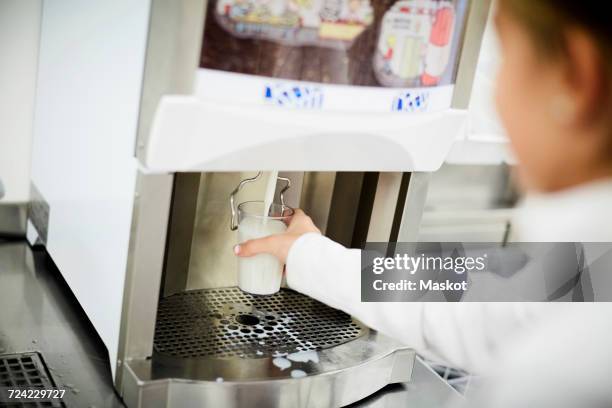 school girl filling glass of milk from machine in school cafeteria - lunchpauze stockfoto's en -beelden