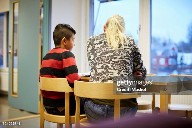 rear view of mid adult teacher teaching boy in classroom - teacher desk stock pictures, royalty-free photos & images