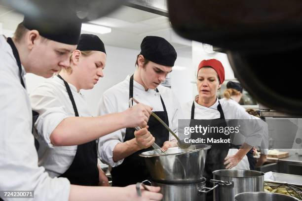 teacher assisting male students in cooking food at commercial kitchen - female whipping stock-fotos und bilder