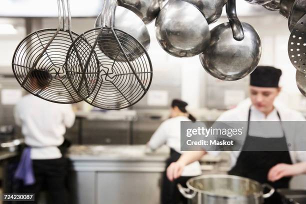 kitchen utensils with chefs cooking in background at commercial kitchen - food and drink establishment stock pictures, royalty-free photos & images