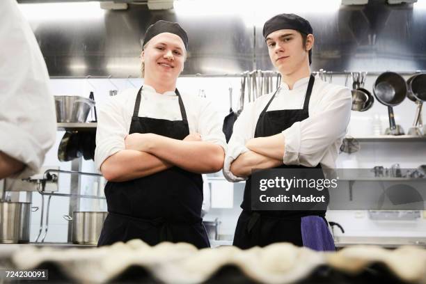 portrait of smiling male chef students standing arms crossed in commercial kitchen - toque stock pictures, royalty-free photos & images