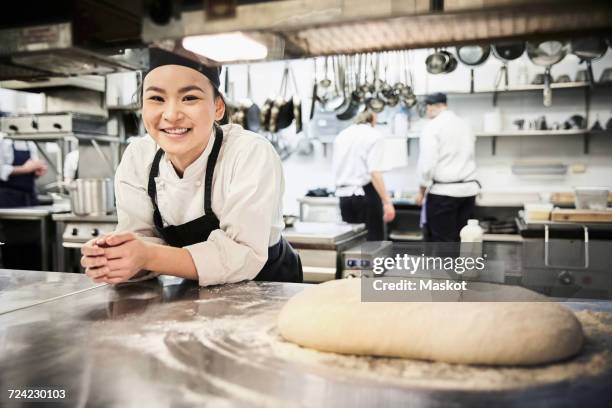 portrait of smiling female chef leaning on counter in commercial kitchen - kochlehrling stock-fotos und bilder