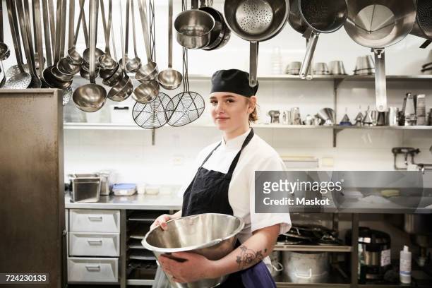 portrait of confident female chef holding container in commercial kitchen - restaurateur photos et images de collection