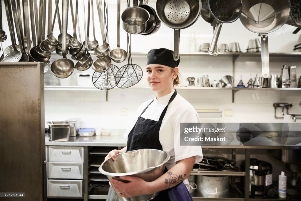 Portrait of confident female chef holding container in commercial kitchen